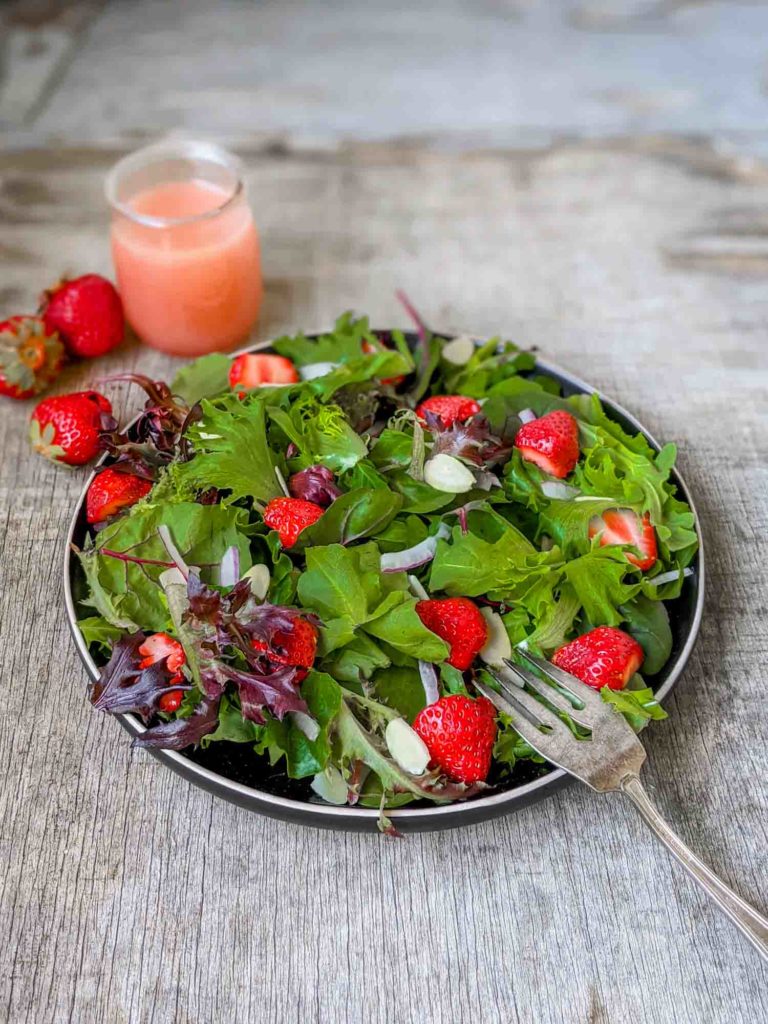 Strawberry salad with spinach, spring mix, arugula, red onion, slivered almonds on a black plate and rustic surface.