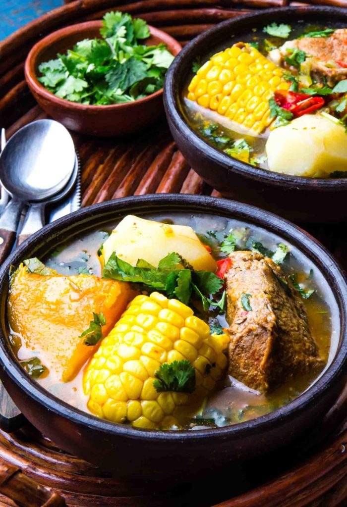 Sancocho Ecuadorian soups in dark bowls with garnishes on table.