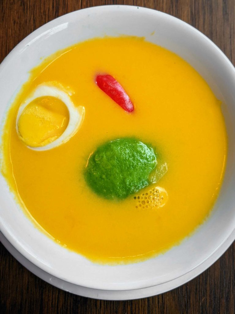 Traditional Ecuadorian soup locro garnished with avocado egg and pepper on a dark background