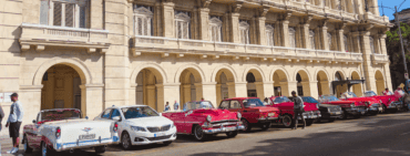 a line of pink convertible classic cars outside building in Havana main plaza