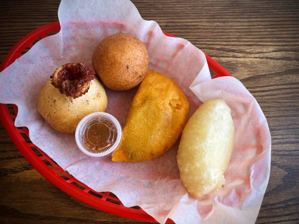 Colombian antojitos pan de guayaba, bunuelo, empanada de carne and carimanola in a red basket with paper