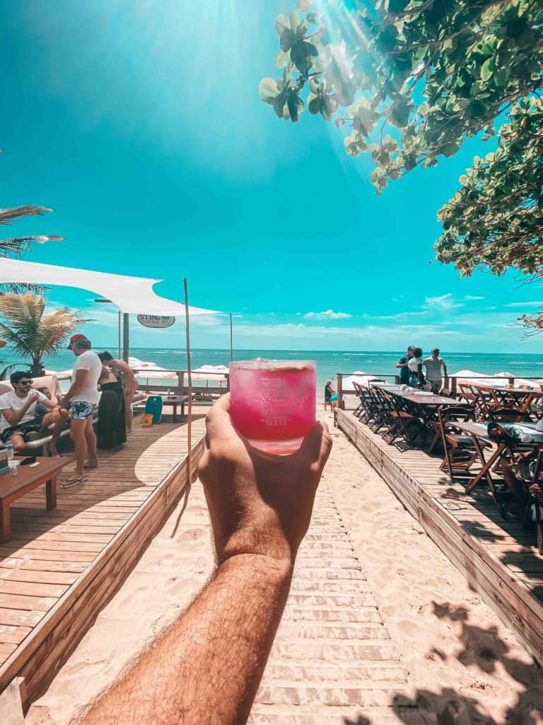 Drinks in Brazil Cobogó in someone's hand walking down a boardwalk to the beach