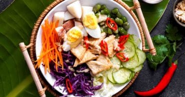 Indonesian gado gado vegetarian food on white plate in bamboo holder on banana leaf and slate