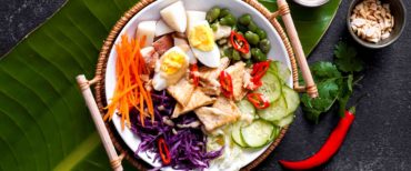 Indonesian gado gado vegetarian food on white plate in bamboo holder on banana leaf and slate