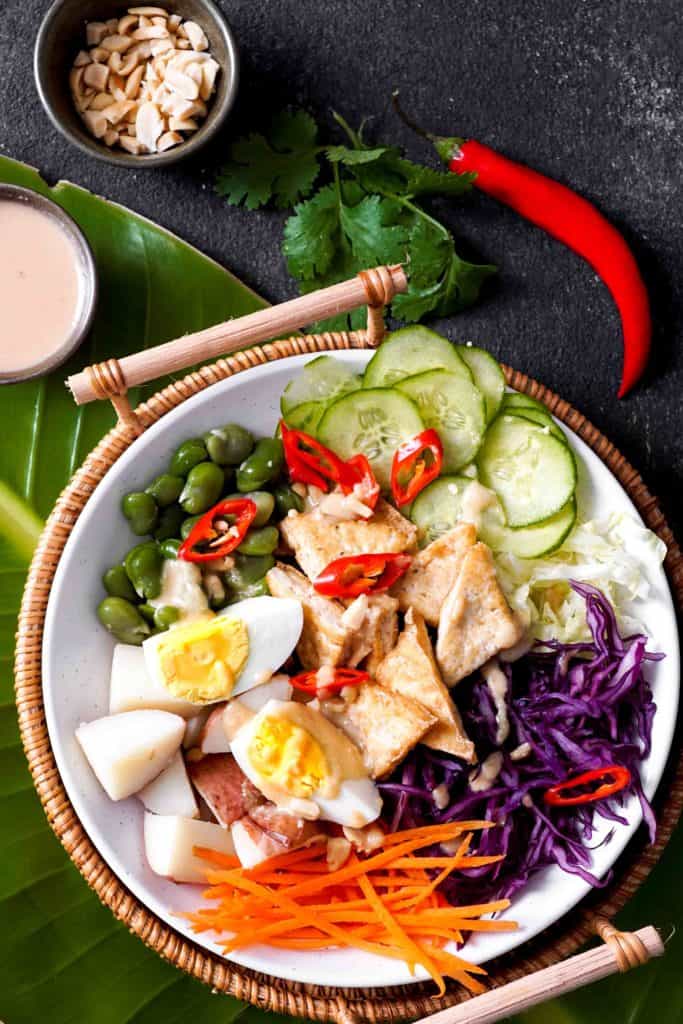 Indonesian gado gado vegetarian food on white plate in bamboo holder on banana leaf and slate