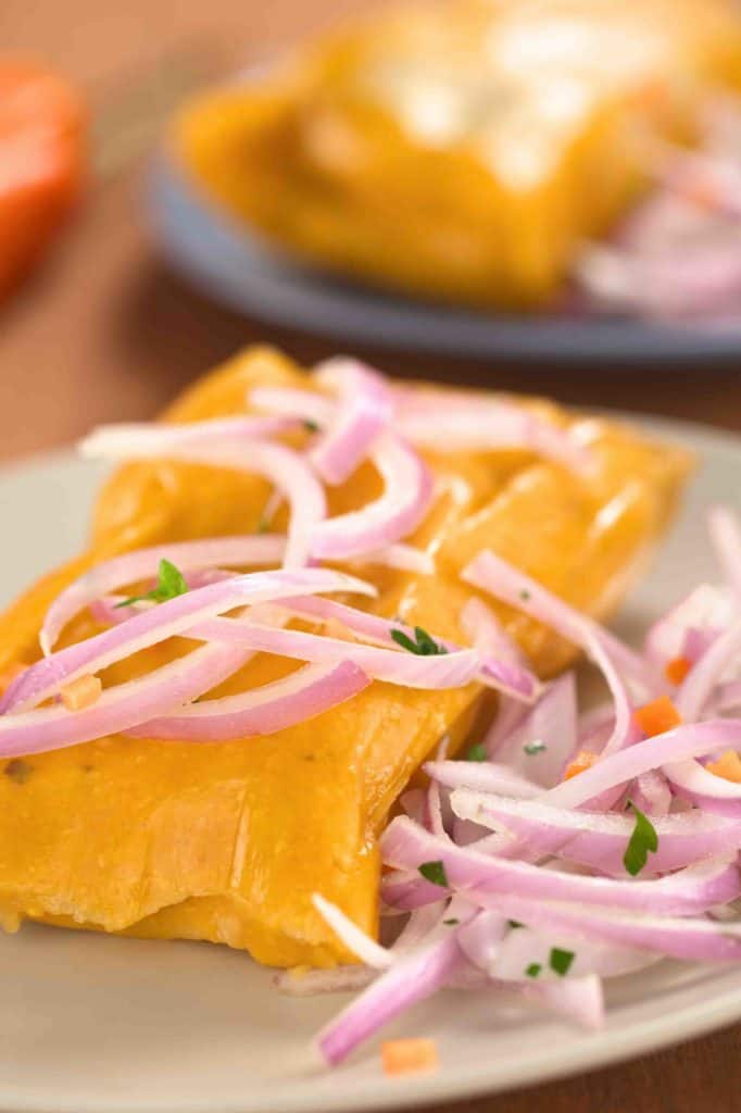 Peruvian tamales (traditionally eaten for breakfast on Sundays) made of corn and chicken and served with salsa criolla (onion salad) (Selective Focus Focus on the front of the onion salad on top of the tamale)