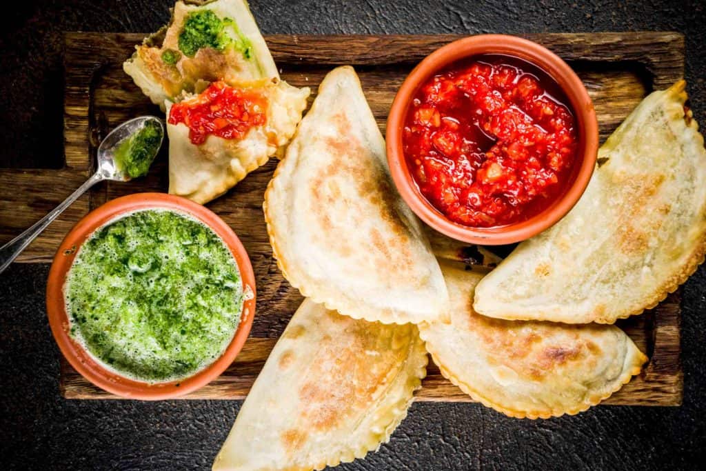 Peruvian empanadas on a wooden tray with dipping sauces