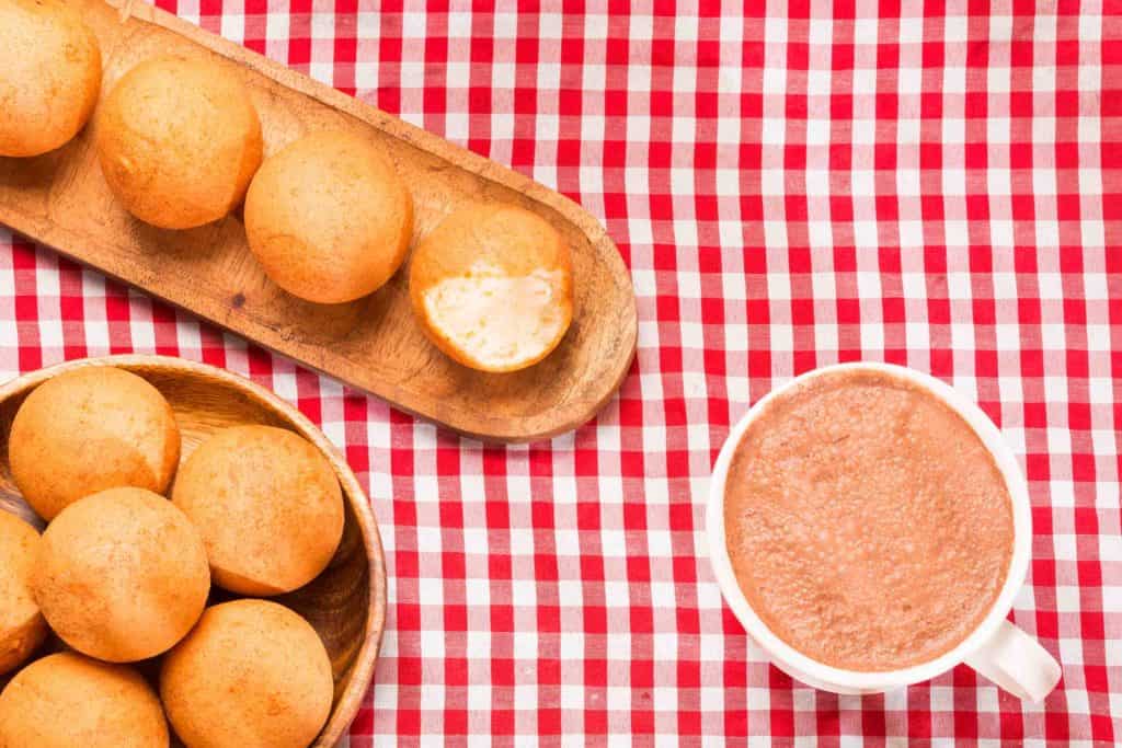 Traditional Colombian buñuelo - Deep Fried Cheese Bread. Hot chocolate drink on red checkered tablecloth