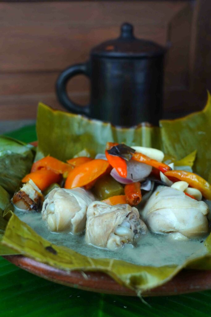 Garang Asem, traditional Javanese food is served on a clay plate, lined with banana leaves and accompanied by a mixture of bird eye chili, tomatoes, shallots, garlic, sour starfruit, and various other spices.