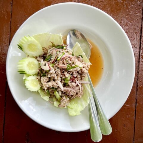 larb moo also known as thai pork salad on a white plate dark table in a Thai restaurant