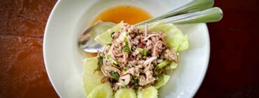 larb moo also known as thai pork salad on a white plate dark table in a Thai restaurant