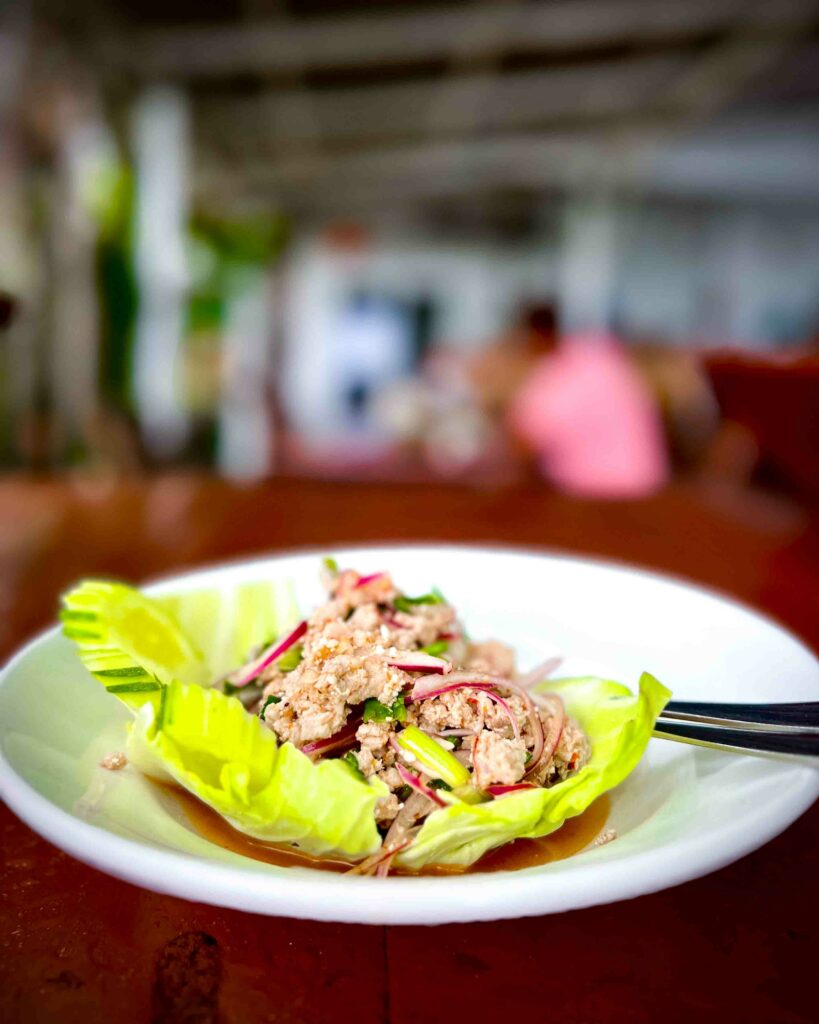 larb moo also known as thai pork salad on a white plate dark table in a Thai restaurant