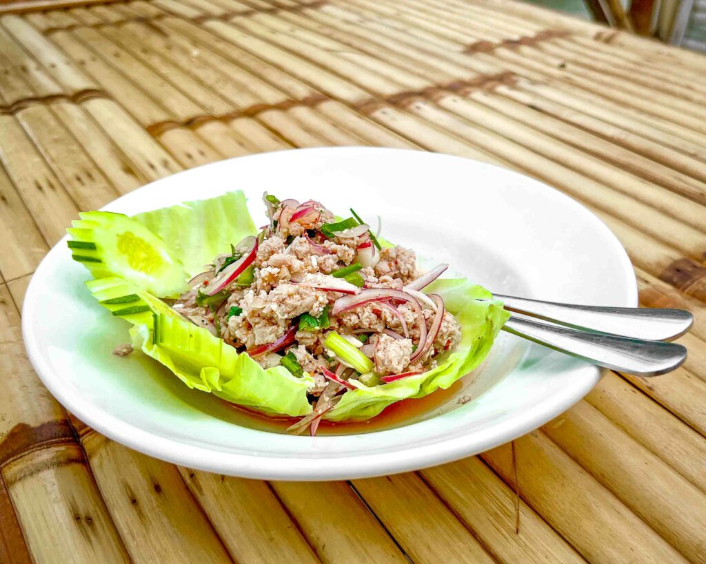 larb moo also known as thai pork salad on a white plate bamboo table in a Thai restaurant