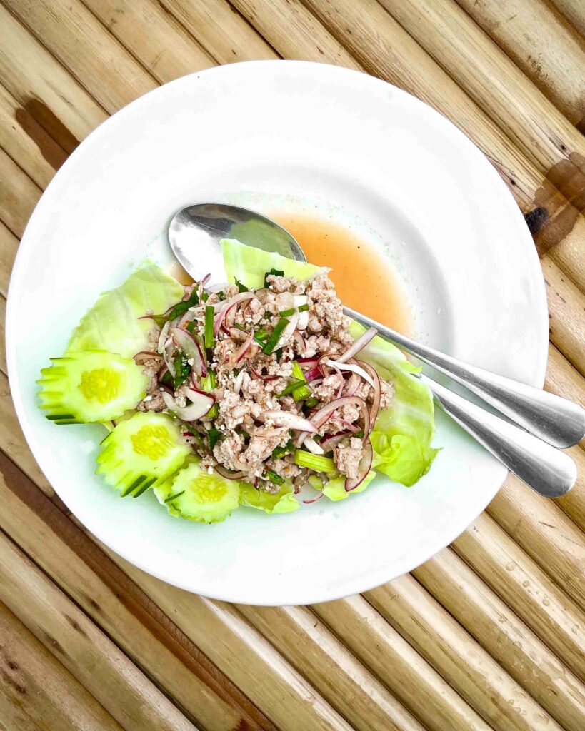 larb moo also known as thai pork salad on a white plate bamboo table in a Thai restaurant