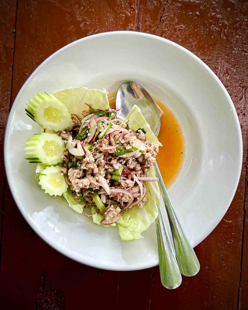 larb moo also known as thai pork salad on a white plate dark table in a Thai restaurant