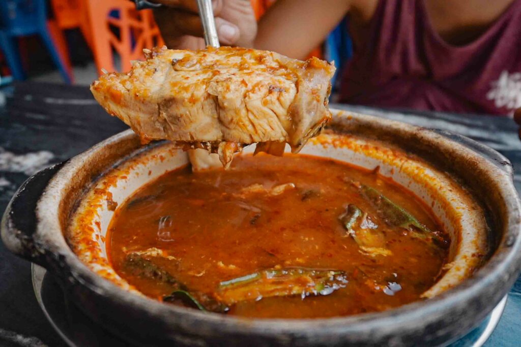 Asam Padeh Ikan in a clay pot this Padang food is a spicy sour fish stew in Padang Indonesia also popular in Malaysia as Asam Pedas.