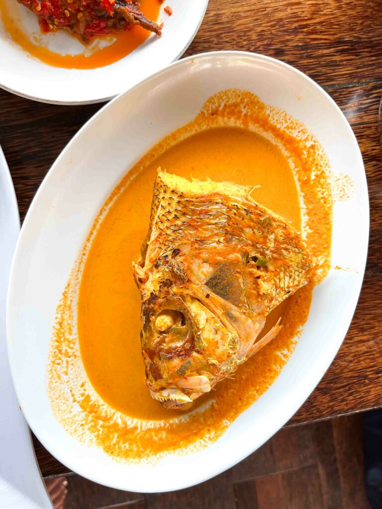 Gulai kepala ikan or fish head curry on a white plate, traditional food in Padang Indonesia