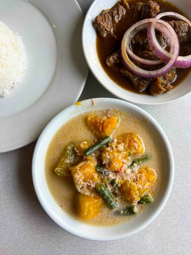 Filipino pumpkin in coconut (Ginataang Calabasa) on a white table with a bowl of beef adobo