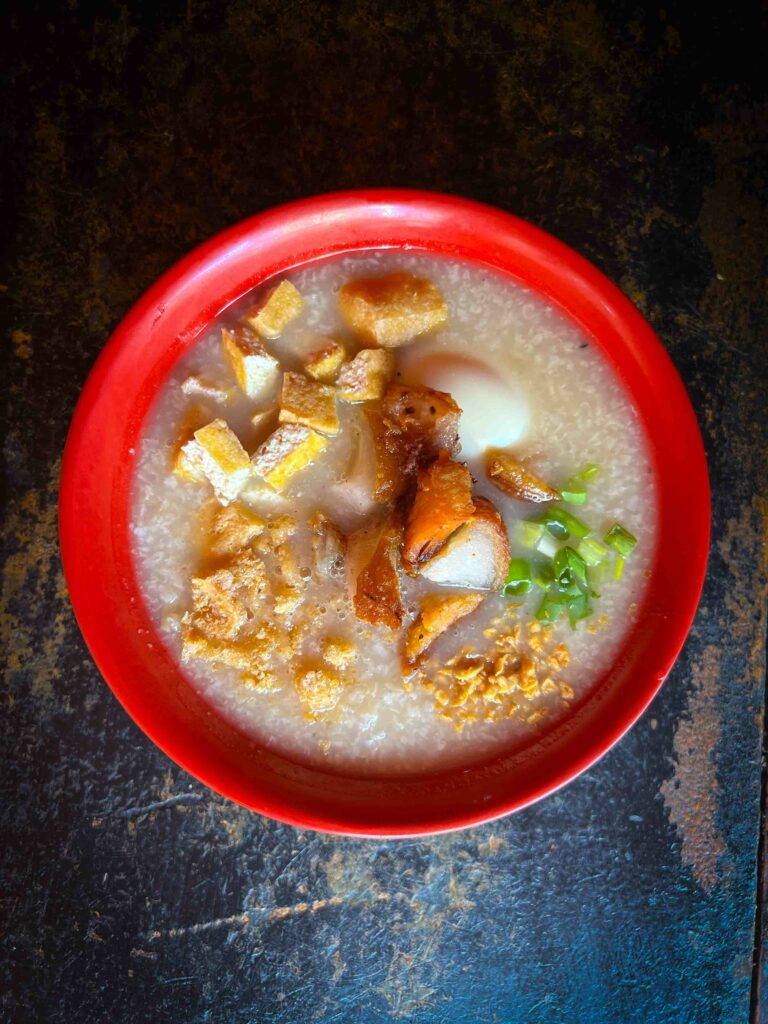 Traditional Filipino breakfast Lugaw in a red bowl on a wooden table