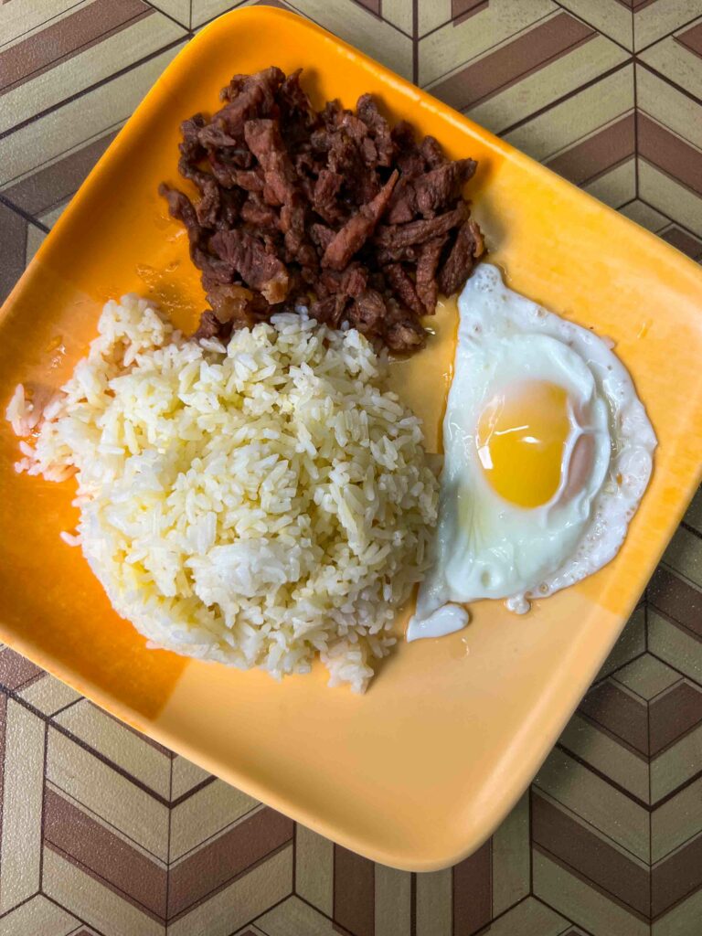Traditional filipino breakfast tapsilog on a yellow plate at a local restaurant
