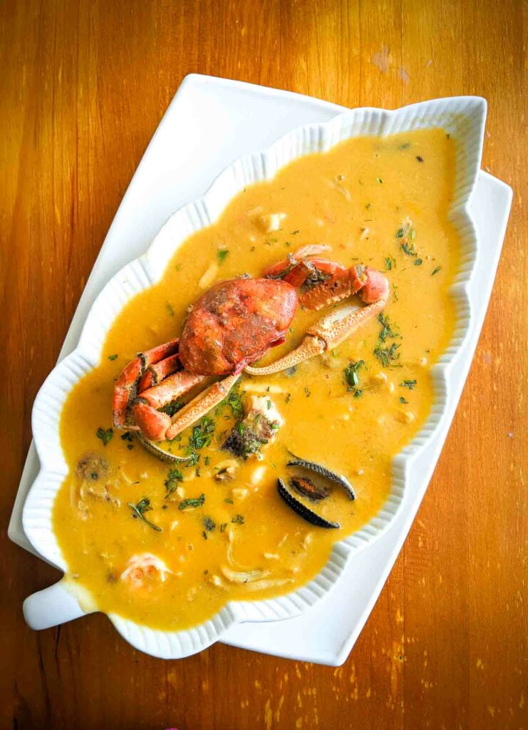 Ecuadorian soup parihuela on a wooden table with seafood in a decorative white plate