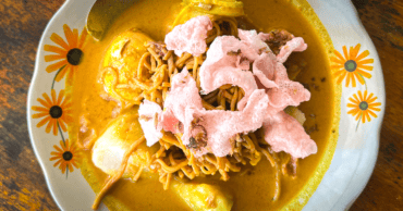 Lontong sayur a traditional Indonesian breakfast of vegetables, compressed rice cake and noodles in a yellow curry. In a white bowl on a wooden table.