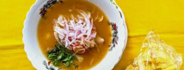 Encebollado traditional Ecuadorian soup with fish and red onion served with a side of plantain chips on a yellow table