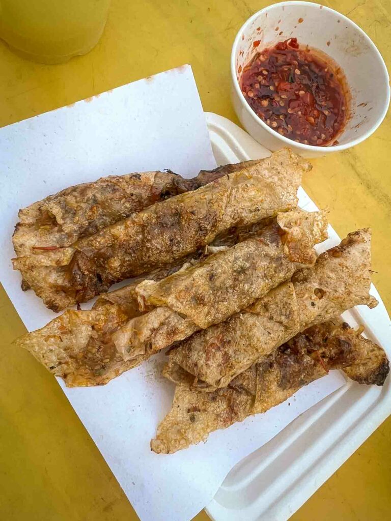 ram cuốn cải special Da nang food. The rolls are small and wrapped in rice paper, then deep-fried until crispy. serves on a paper on yellow table with dipping sauce