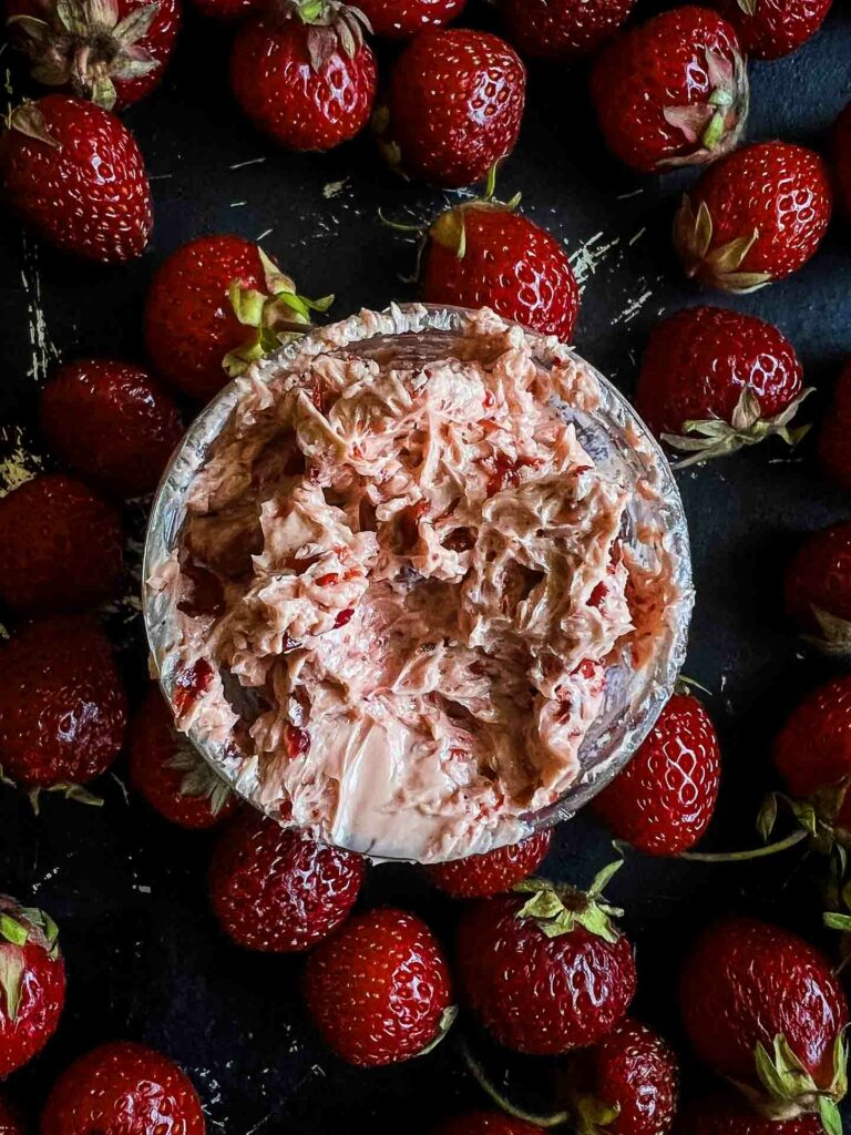 spicy strawberry butter with strawberries surrounding it on a black background