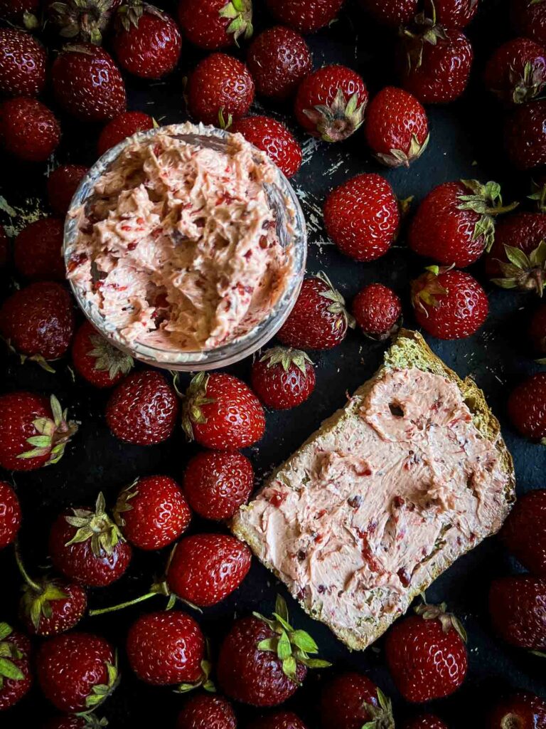 spicy strawberry butter alongside buttered bread with strawberries surrounding it on a black background