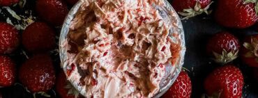 Whipped strawberry chipotle butter in the middle of a bunch of loose strawberries on a black baking sheet