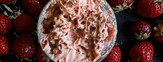 Whipped strawberry chipotle butter in the middle of a bunch of loose strawberries on a black baking sheet