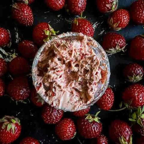 Whipped strawberry chipotle butter in the middle of a bunch of loose strawberries on a black baking sheet