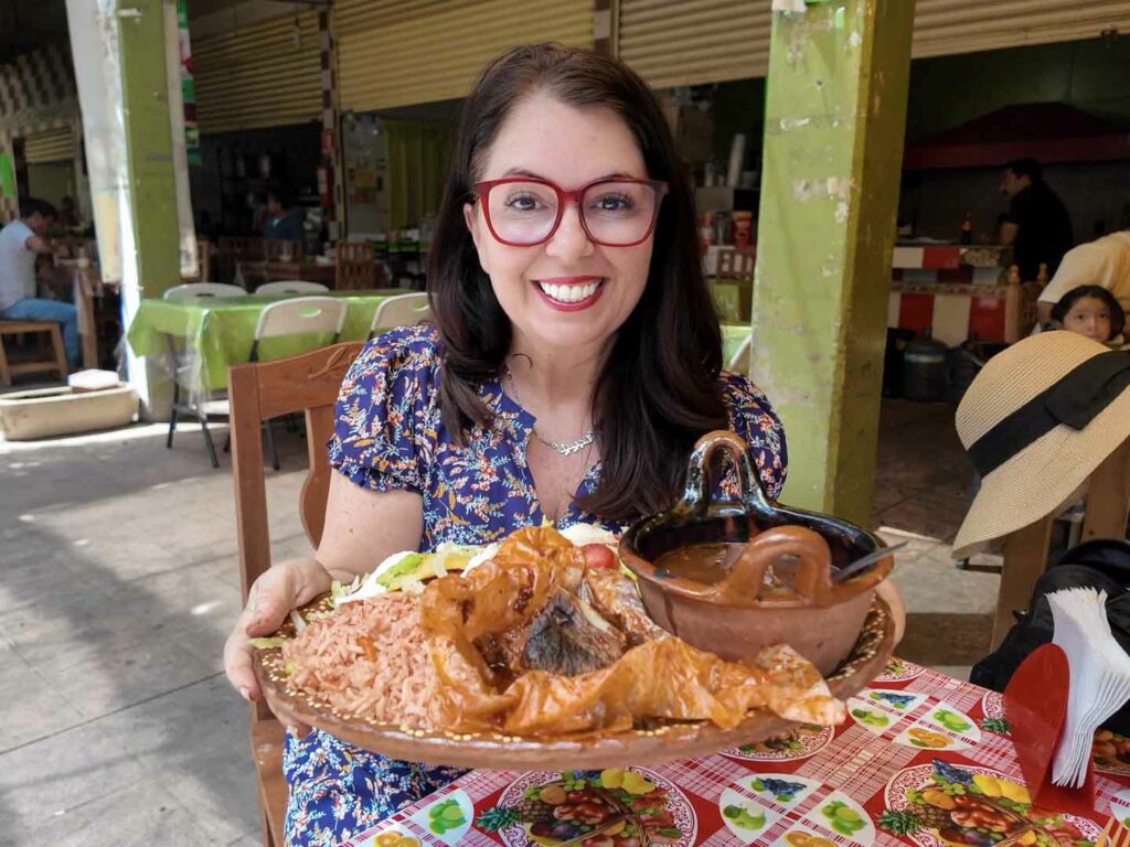 Ayngelina holding mixiote de borrego in Tlaxcala Mexico at the local market fonda, it is made by steaming lamb in the membrane of an agave and served with many sides, a traditional dish in Tlaxcala