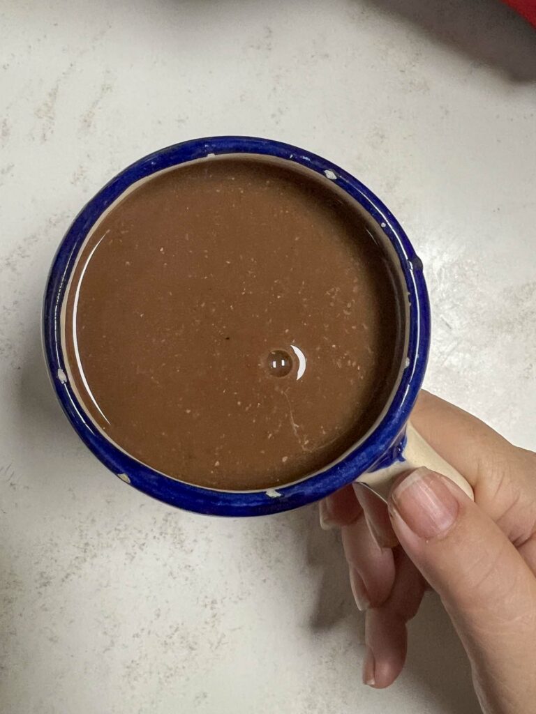 champurrado Mexican drink made with corn and cacao, in woman's hand on table