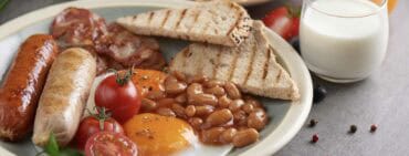 Traditional full English breakfast with fried eggs, sausage, tomato, beans, toast and bacon on a plate,