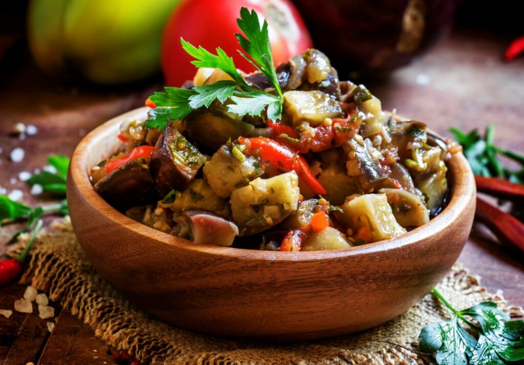 Ajapsandali Georgian food , a vegetable stew of eggplant peppers, tomato and onion on a wooden table with ingredients in the background