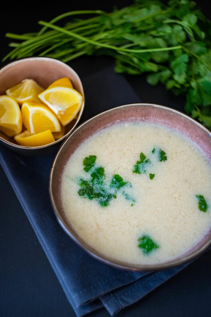 Chikhirtma Georgian food, clear chicken soup thickened with egg and lemon. In a bowl garnished with cilantro on a black table with a bowl of lemons and more cilantro