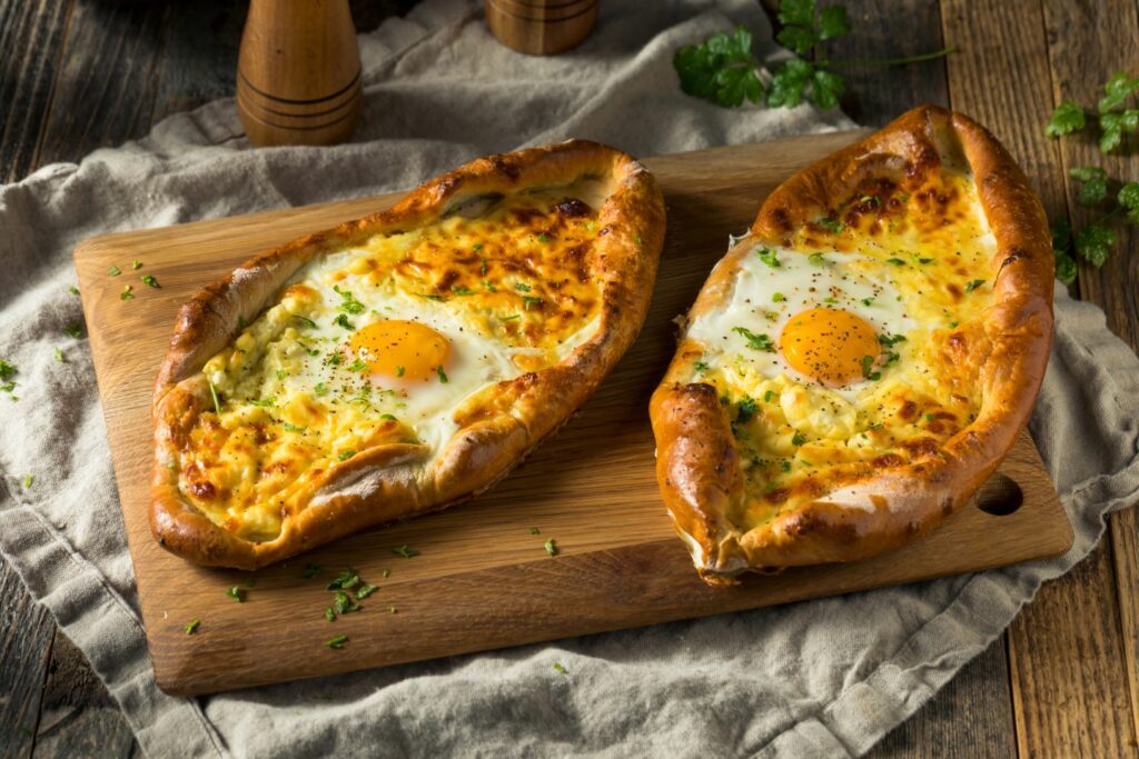 Khachapuri is cheese bread you will see a lot. It comes in regional versions like Adjarian with an egg on top like this one on a wooden cutting board with a linen cloth underneath a rustic table setting