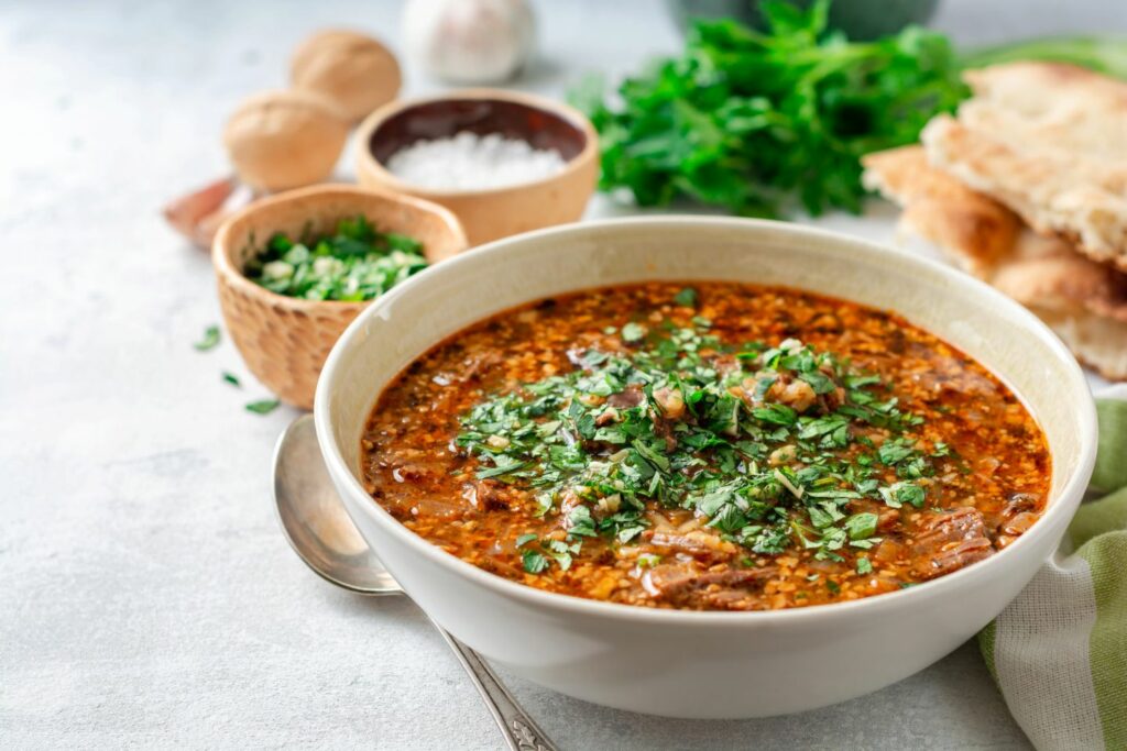 Georgian kharcho A spicy beef rice soup with plum paste and walnuts in some versions. On a white table with ingredients in the background.