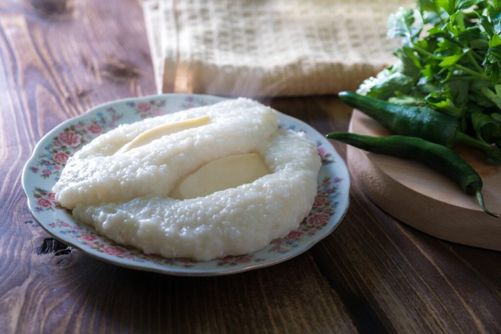 Ghomi in Georgia, a coarse cornmeal porridge on a vintage plate with a rustic wooden table and peppers and greens aside.