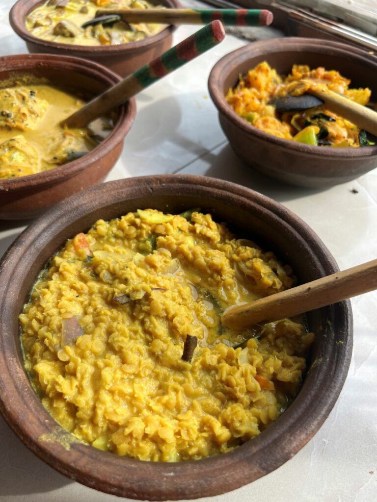 Sri Lankan Dal curry in a wooden bowl with spoon and traditional dishes in background 