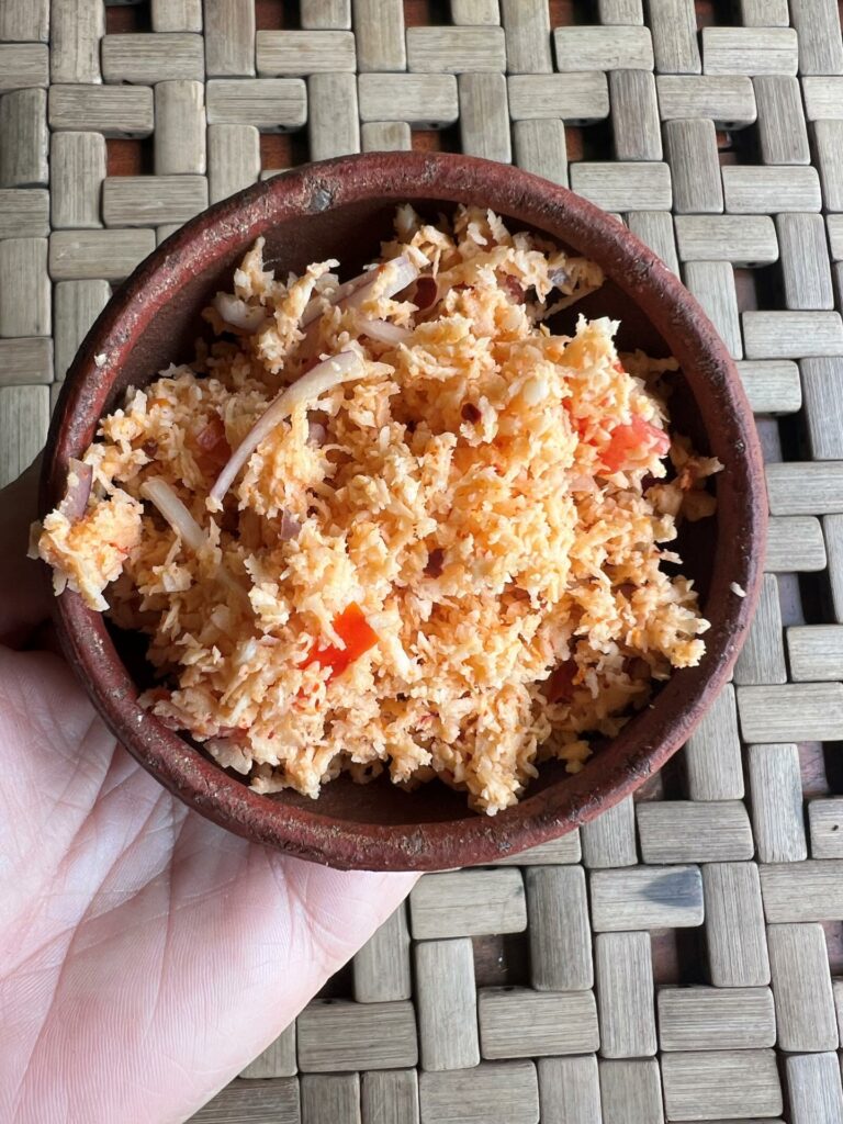 Pol Sambol or Sri Lankan  Coconut Relish in a brown bowl in a woman's hand over a rattan background